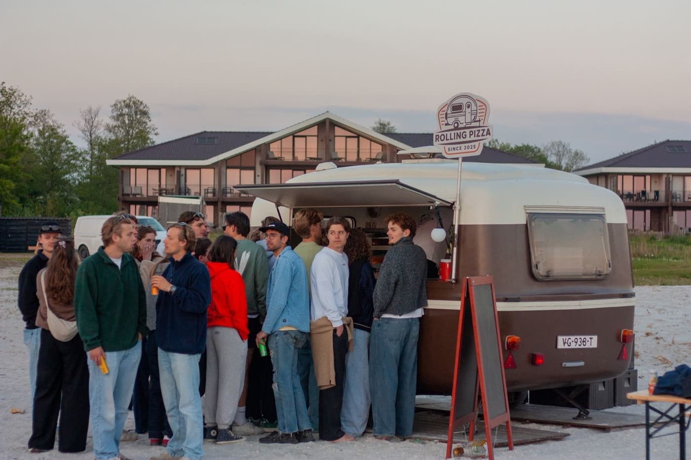 Drukke rij gasten bij de Rolling Pizza caravan tijdens een avondevenement